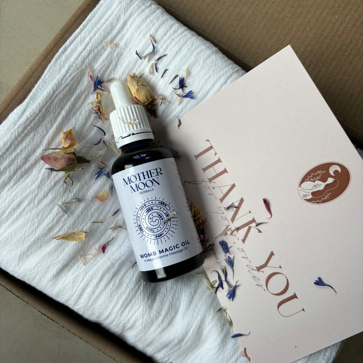 Bottle of Mother Moon Womb Magic Oil on a textured surface with a 'Thank You' card.